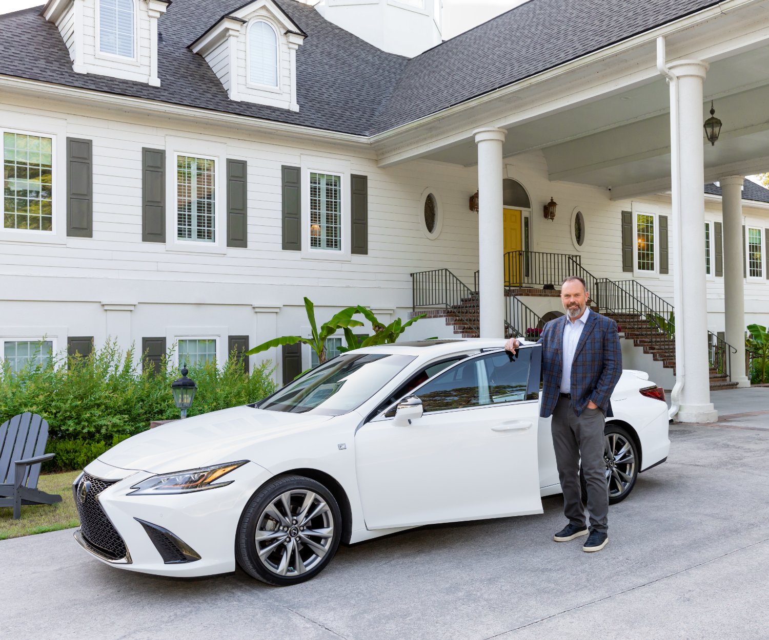 Ken Strange, founder of Ride to Hope, standing beside a white Lexus sedan in front of a treatment center.